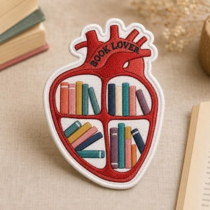 May include: An embroidered patch shaped like an anatomical heart with a white border. The interior is divided into four sections containing rows of colorful books. The text BOOK LOVER is stitched in black thread across the top of the heart.