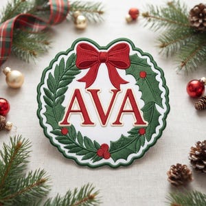 May include: A circular embroidered patch featuring a white center with the red text AVA, surrounded by a green holly wreath and a red bow at the top. The patch has a scalloped edge and is displayed against a neutral fabric background.