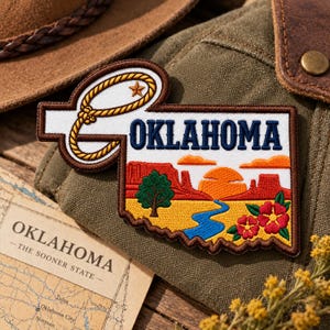May include: An embroidered patch shaped like the state of Oklahoma featuring a yellow rope lasso, a small star, the text OKLAHOMA, and a landscape scene with red mesas, a green tree, a blue river, and red flowers on a white background.