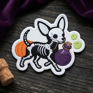 May include: An embroidered patch featuring a black and white skeleton dog with large ears, carrying a purple potion bottle in its mouth. Behind the dog is an orange pumpkin, and two small green bubbles float near the bottle on a white background.