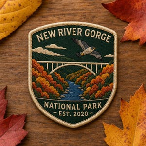 May include: A shield-shaped embroidered patch featuring a dark green background with a white arched bridge over a blue river, surrounded by orange and yellow autumn trees. A bird flies above the bridge. Text reads NEW RIVER GORGE NATIONAL PARK EST. 2020.