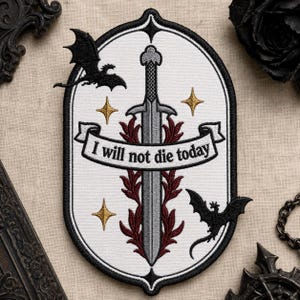 May include: An oval embroidered patch featuring a central silver sword flanked by dark red foliage. A white banner across the center displays the black text "I will not die today." Two black dragons and four gold stars surround the sword.