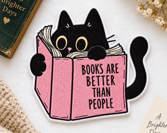 Può includere: Una toppa ricamata raffigurante un gatto nero con grandi occhi gialli che tiene in mano un libro rosa aperto. La copertina del libro riporta il testo nero "BOOKS ARE BETTER THAN PEOPLE". Il gatto ha una lunga coda nera ed è intento a leggere.