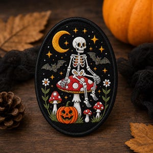 May include: An oval embroidered patch featuring a white skeleton sitting on a large red and white spotted mushroom. The design includes a yellow crescent moon, gold stars, two grey bats, a carved orange jack-o'-lantern, and small red mushrooms.