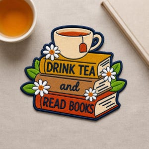 May include: An embroidered patch featuring a stack of three books with a tea cup on top. The books are yellow, brown, and orange with the text "DRINK TEA and READ BOOKS" in dark blue. White daisies with yellow centers and green leaves decorate the stack.
