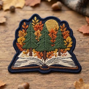 May include: An embroidered patch featuring an open book with pages fanned out at the bottom. Three green pine trees rise from the center of the book, surrounded by orange and yellow autumn leaves. A yellow sun sits in the dark blue sky background.