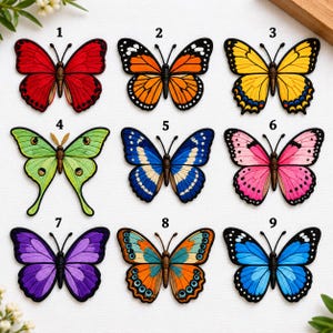 May include: A collection of nine butterfly-shaped patches arranged in a grid, numbered one through nine. Each patch features distinct color patterns including red, orange, yellow, lime green, blue, pink, purple, and teal, all with black outlines.
