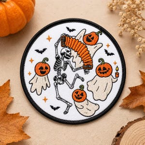 May include: A circular embroidered patch with a white background and a black border. The design features a skeleton playing an orange accordion, surrounded by three ghosts with orange jack-o'-lantern heads, small black bats, and orange stars.