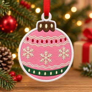May include: A round, pink embroidered Christmas ornament featuring white snowflake patterns, wavy lines, and a dark green band with white dots. The ornament has a brown cap at the top and is suspended by a red ribbon loop for hanging on a tree.