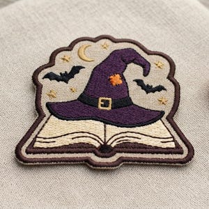 May include: An embroidered patch featuring an open book with a purple witch hat resting on top. The hat has a black band with a gold buckle and an orange patch. The background includes a yellow crescent moon, small yellow stars, and two black bats.