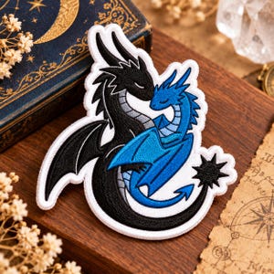 May include: An embroidered patch featuring two dragons with their heads touching. One dragon is black with grey underbelly details, and the other is blue with lighter blue accents. The patch has a white border and a black star-shaped tail tip.