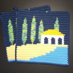 Könnte beinhalten: Zwei marineblaue gehäkelte Topflappen mit Landschaftsdesign. Das Design zeigt gelbes und blaues Wasser, ein gelbes Gebäude mit weißen Säulen und grüne und blaue Bäume. Jeder Topflappen hat eine Schlaufe zum Aufhängen.