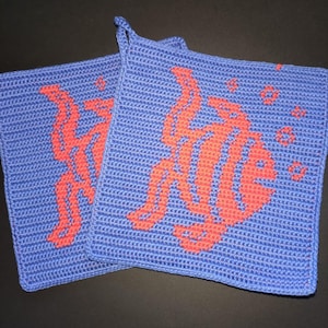 Könnte beinhalten: Zwei blaue gehäkelte Topflappen mit einem korallenfarbenen Fischmuster. Jeder Topflappen hat eine Schlaufe zum Aufhängen. Das Fischdesign umfasst Details wie Flossen und Blasen und verleiht der Küche eine dekorative Note.