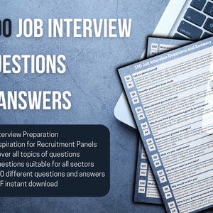 Puede incluir: Un documento azul y blanco con el texto "100 Job Interview Questions and Answers" sobre un fondo blanco. El documento está doblado por la mitad y la mitad superior es visible. El documento está en una computadora portátil con un teclado gris.