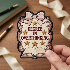 May include: An embroidered patch with a cream background, a black border, and a pink bow at the top. It features the text "DEGREE IN OVERTHINKING" in maroon, surrounded by six gold stars and an open book at the bottom, all framed by pink scrollwork.