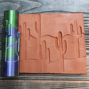 Peut inclure: Un rouleau à pâtisserie vert et bleu avec un motif de cactus. Le rouleau à pâtisserie est utilisé pour créer une empreinte du motif de cactus sur une tuile en terre cuite.