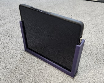 Op de afbeelding: Een paarse tabletstandaard met een zwarte tablet erin. De standaard is gemaakt van plastic en heeft een eenvoudig ontwerp.