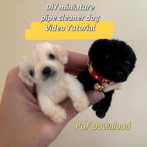 May include: Two miniature pipe cleaner dogs, one cream-colored and one black, are held in a hand. The cream-colored dog has a light brown head and ears. The black dog wears a red collar with a gold bell. Text reads "DIY miniature pipe cleaner dog Video Tutorial" and "PDF Download."