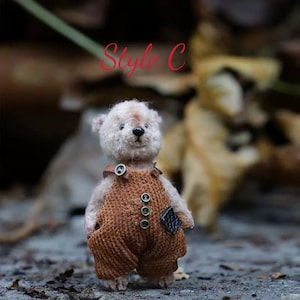 Pu&ograve; includere: Un piccolo orsacchiotto di peluche fatto a mano con un manto marrone chiaro e soffice. L'orso indossa una salopette marrone con una toppa sulla tasca. L'orso &egrave; in piedi su una superficie marrone strutturata. Il testo "Style C" &egrave; visibile sullo sfondo.