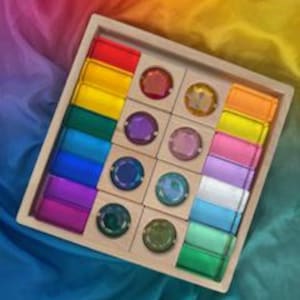 May include: Wooden toy set with a rainbow of colored blocks and circular gems. The blocks are rectangular and arranged in a wooden tray. The gems are circular and have a reflective surface. The colors include red, orange, yellow, green, blue, and purple.