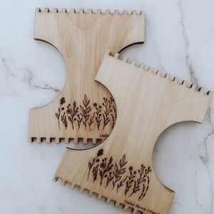 K&ouml;nnte beinhalten: Zwei Holzwebst&uuml;hle mit einem Blumendesign und dem Text "Cedar Brook Fiber Co."
