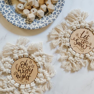 May include: Two wooden Christmas decorations with macrame fringe. One decoration says "Oh Holy Night" and the other says "Let it Snow".