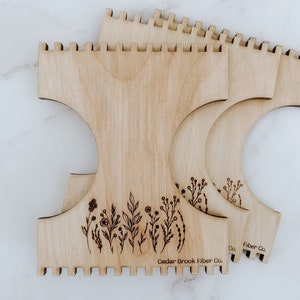 K&ouml;nnte beinhalten: Drei Holz-Webrahmen mit einem Blumenmuster und dem Text "Cedar Brook Fiber Co.".