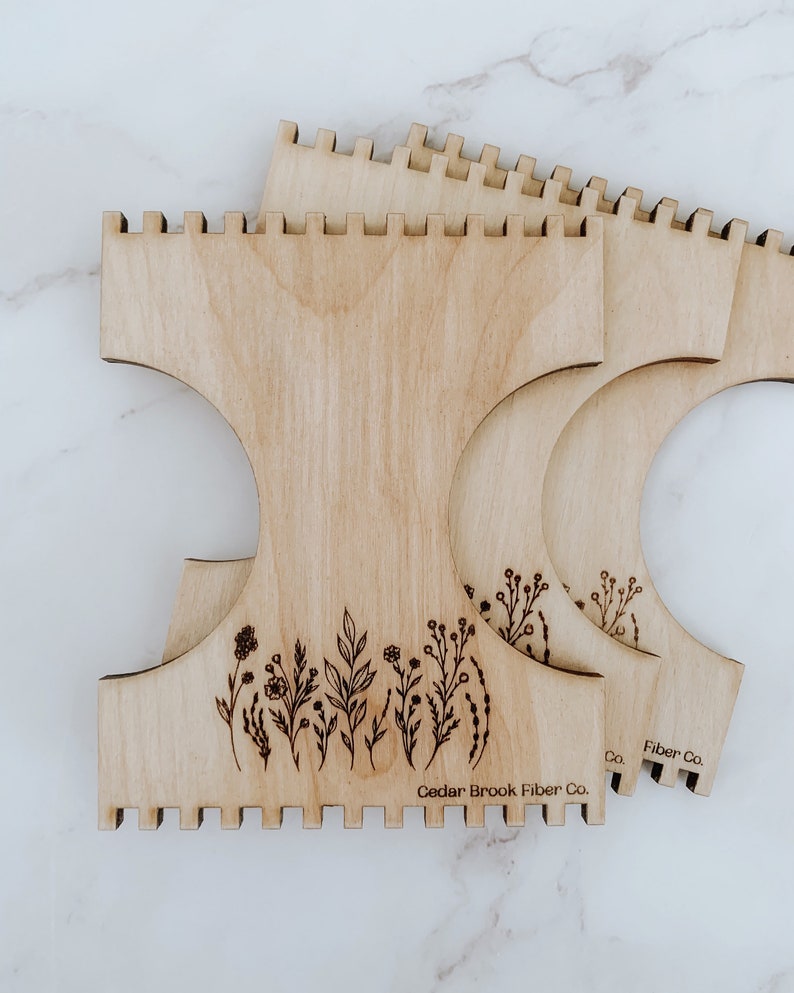 K&ouml;nnte beinhalten: Drei Holz-Webrahmen mit einem Blumenmuster und dem Text "Cedar Brook Fiber Co.".