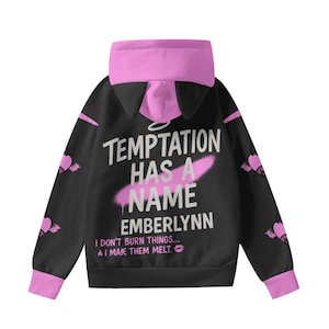 May include: Black hoodie with pink accents, featuring the text "TEMPTATION HAS A NAME EMBERLYNN". The hoodie has a pink hood and cuffs, with bat-wing designs on the sleeves. The text "I DON'T BURN THINGS... I MAKE THEM MELT" is also printed on the hoodie.