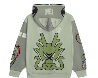 Può includere: Una felpa con cappuccio verde salvia con una grande grafica di drago verde sul retro. Il cappuccio presenta la scritta "MEI" e orecchie stilizzate. Disegni a tema drago adornano le maniche. È un capo casual.