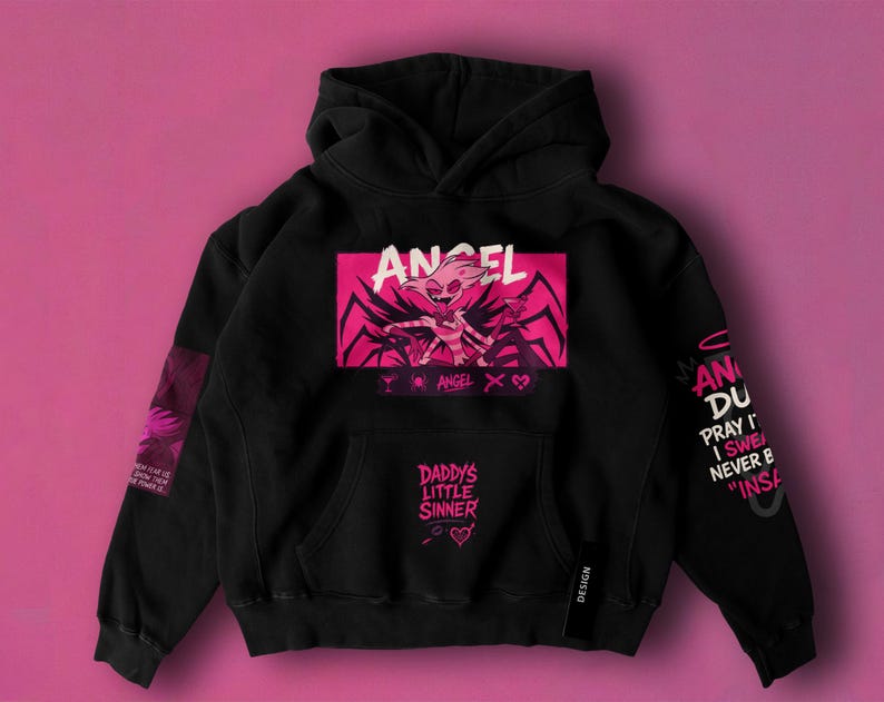 May include: Black hoodie with a pink and white graphic of a character and the word "ANGEL". The hoodie has the text "DADDY'S LITTLE SINNER" on the front pocket and text on the sleeves. The background is a solid pink color.