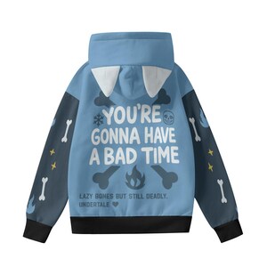 May include: A light blue hoodie with a high collar and a hood featuring white accents. The back displays the text "YOU'RE GONNA HAVE A BAD TIME" with bone and skull graphics. The sleeves have bone and star patterns.