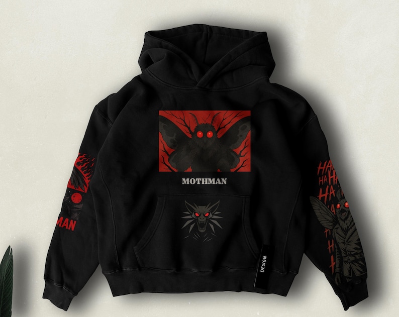 Cryptid-themed Mothman hoodie featuring the mysterious winged figure with glowing red eyes, silhouetted against a dark sky or bridge scene, perfect for fans of paranormal legends and eerie aesthetics.