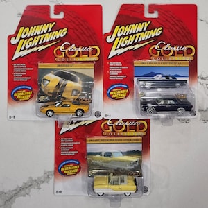 May include: Three die-cast model cars from the Johnny Lightning Classic Gold Collection. The models include a yellow 2005 Ford GT, a black 1961 Lincoln Continental, and a yellow 1961 AMC Metropolitan Convertible. Each car is in its original packaging.