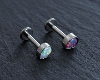 Puede incluir: Dos piezas de joyería corporal plateadas con piedras de ópalo en forma de lágrima. Una piedra es un ópalo azul claro y la otra es un ópalo morado.