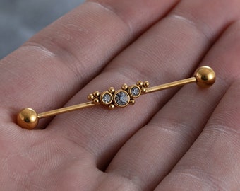 Op de afbeelding: Gouden barbell met een cluster van heldere edelstenen in het midden.