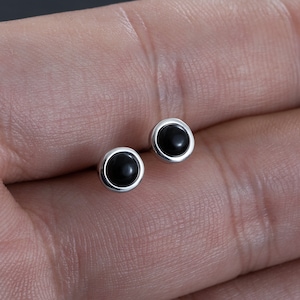 Puede incluir: Un par de pendientes de plata con piedras redondas negras.