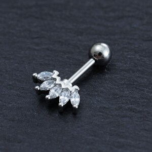 May include: Silver body piercing with a clear crystal crown design. The crown is made of small, marquise-shaped crystals.