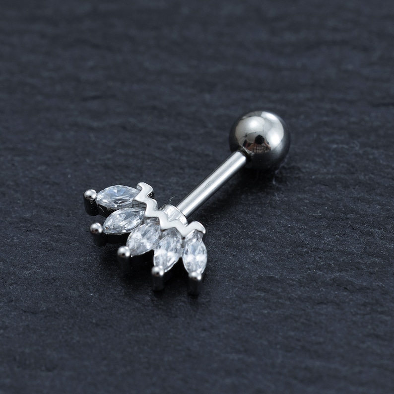 May include: Silver body piercing with a clear crystal crown design. The crown is made of small, marquise-shaped crystals.