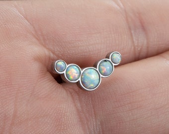 Puede incluir: Una pieza de joyería corporal de plata con cinco piedras de ópalo en forma de curva.