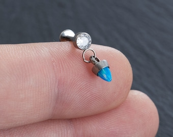 Puede incluir: Un piercing corporal plateado con una parte superior de cristal transparente y un colgante de ópalo azul.
