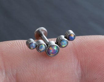 Puede incluir: Un piercing corporal de plata con una fila curva de cinco piedras de ópalo iridiscente.