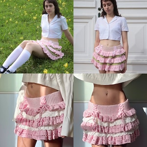 Puede incluir: Una falda de crochet rosa y blanca con múltiples capas de volantes. La falda está hecha con un hilo delicado y tiene un diseño femenino y caprichoso.