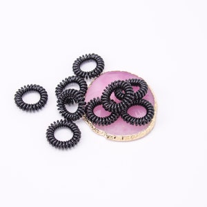 Könnte beinhalten: Eine Gruppe schwarzer Spiral-Haargummis auf einem rosa und goldenen Achat-Untersetzer.