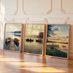 May include: Three framed landscape art prints. The first shows two wooden boats docked on a pier. The second depicts silhouettes of people in boats on a lake. The third shows a sunset over a lake with people on a dock.