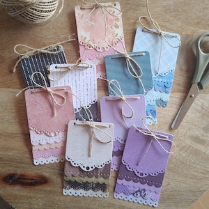 Può includere: Una collezione di dieci etichette regalo fatte a mano con vari disegni e colori. Le etichette sono fatte di carta e hanno un bordo a festoni. Ogni etichetta ha un foro nella parte superiore per una corda o un nastro.