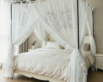 May include: A four-poster bed draped with white lace curtains. The bed frame is dark brown, and the bedding is a neutral beige. The curtains are tied back with white ribbons, creating a romantic and airy feel. A small plant sits on the nightstand.
