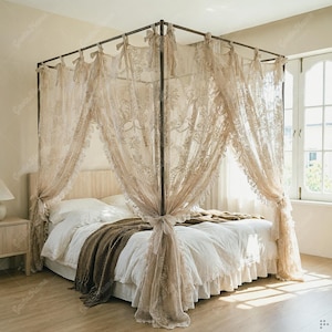 May include: A four-poster bed frame draped with sheer, beige lace curtains featuring intricate floral embroidery. The bed is dressed in white bedding with a dark brown knit throw blanket, and the curtains are secured to the frame with fabric ties.