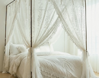 May include: A white canopy bed with sheer, lacy curtains and matching bedding. The bed frame is a dark brown color, and the curtains are tied back with ribbons. The bedding includes a comforter, pillows, and a bed skirt, all in white.