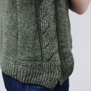 Könnte beinhalten: Ein ärmelloses Strickoberteil in dunkelgrün mit einem detaillierten Zopfmuster an der Seite.